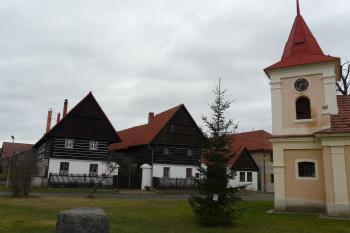 kaple a roubené domy na návsi, vlevo v popředí kamenný blok 