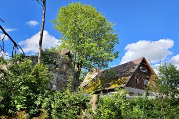 Celkový pohled na skalní bradlo, po němž je pojmenována celá ves, a starší část bývalé sklárny (© Jan P. Štěpánek  05/2024)