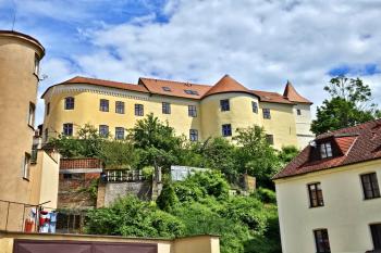 Celkový pohled na dům Na Puši s půlválcovou věží staré novoměstské hradby i mladší hranolovou vodárenskou věží z náměstí U Vodárny (© Jan P. Štěpánek  05/2024)