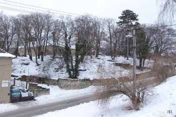 Celkový pohled na výběžek, kde stával zámek. Podél silnice zachovaná zeď opevnění s okrouhlou baštou. ( © Roman Řezáč 03/2005)